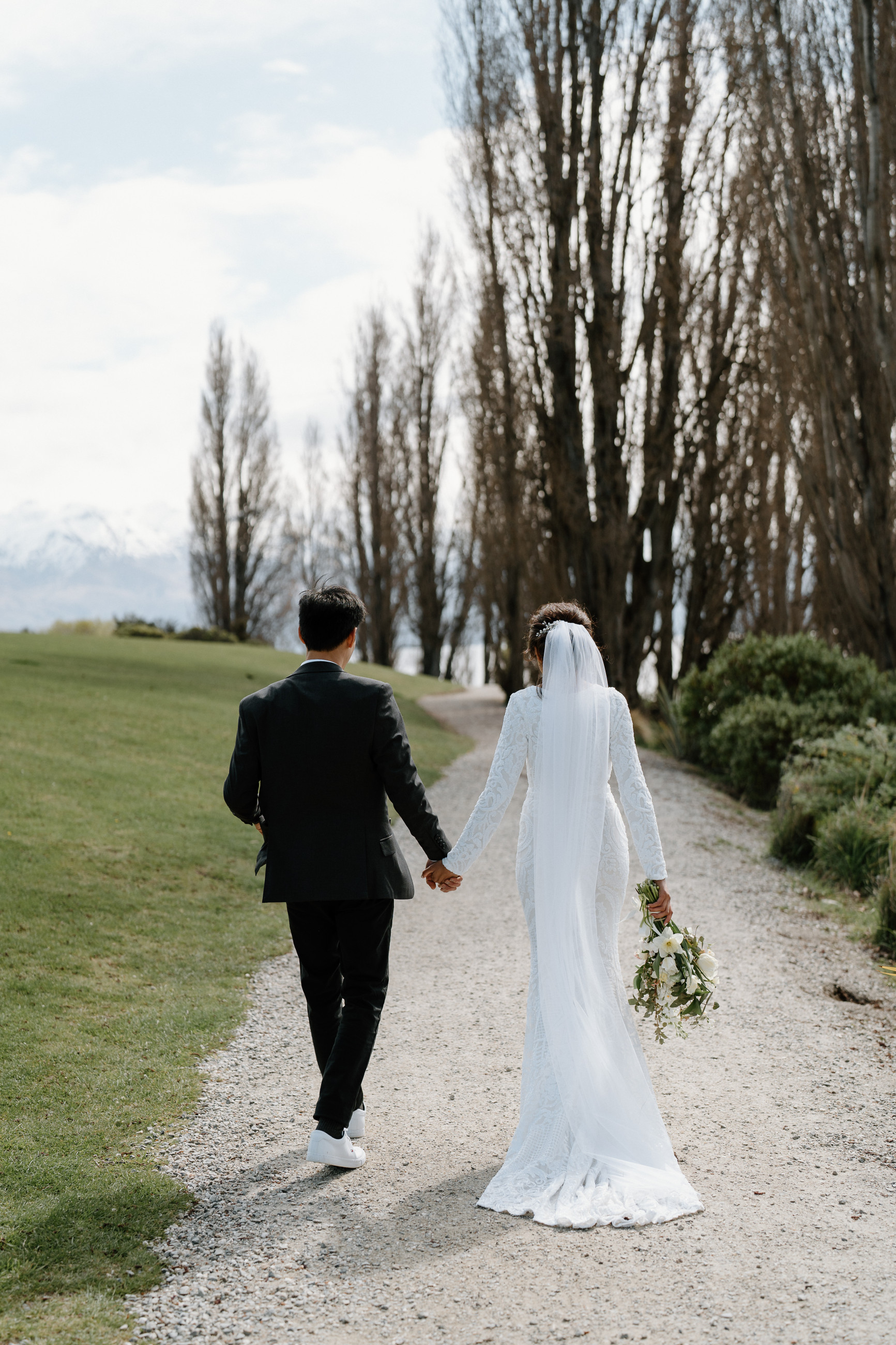 Bride and Groom holding hands walking away from the camera along the Millennium walkway in Front of Edgewater Lake Wānaka