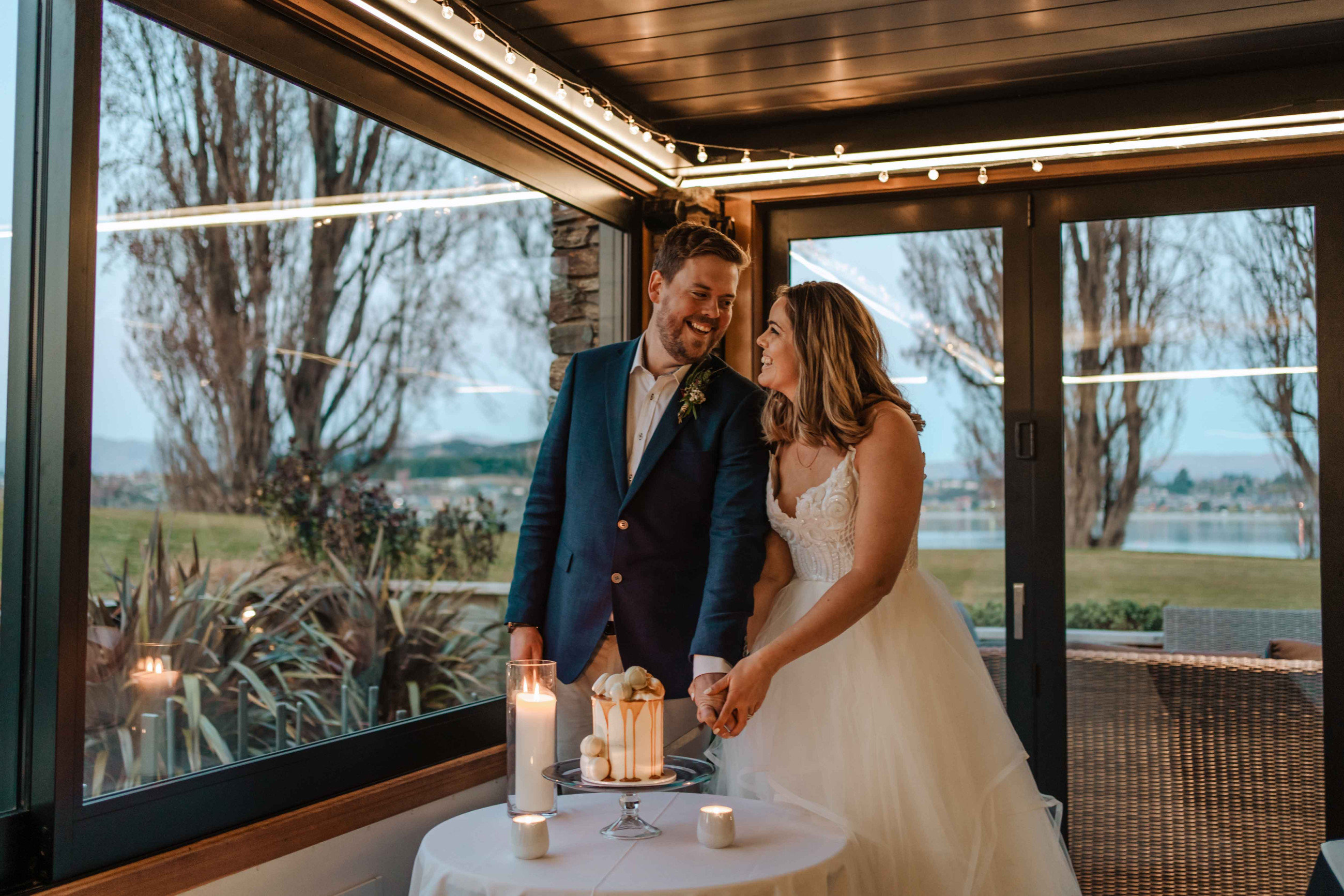 Bride and groom smiling at each other cutting their wedding cake. They are in Edgewater's Alcove and it's softly lit by candle light